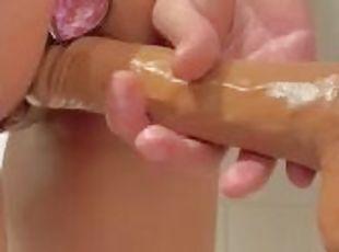 Petite girl with butt plug fucking a wall mounted dildo in the bath...