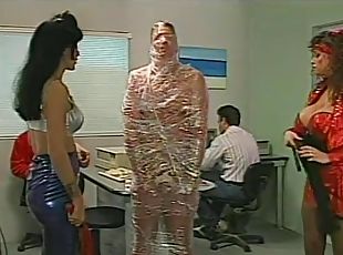 Mistresses cover a man in tight plastic wrap